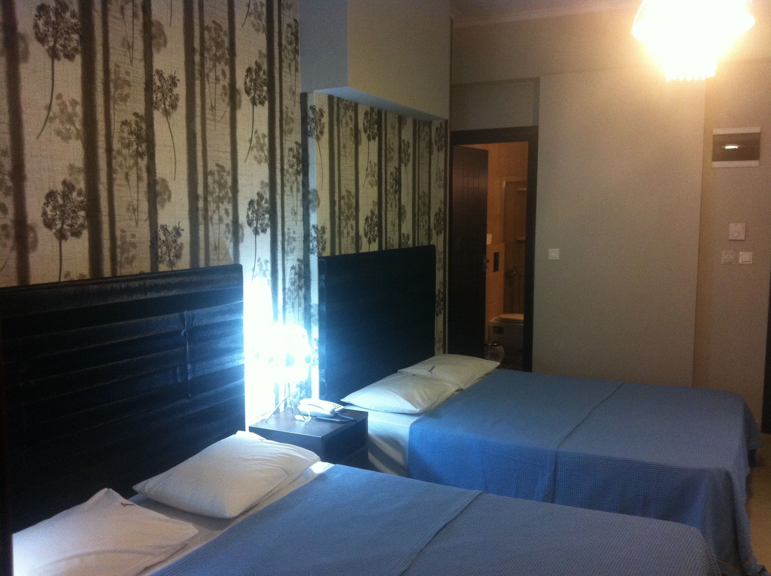 A hotel room with two beds, a nightstand, a lamp, and a door leading to a bathroom.
