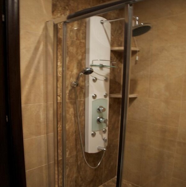A glass-enclosed shower stall with a control panel, a handheld showerhead, and a wall-mounted faucet.