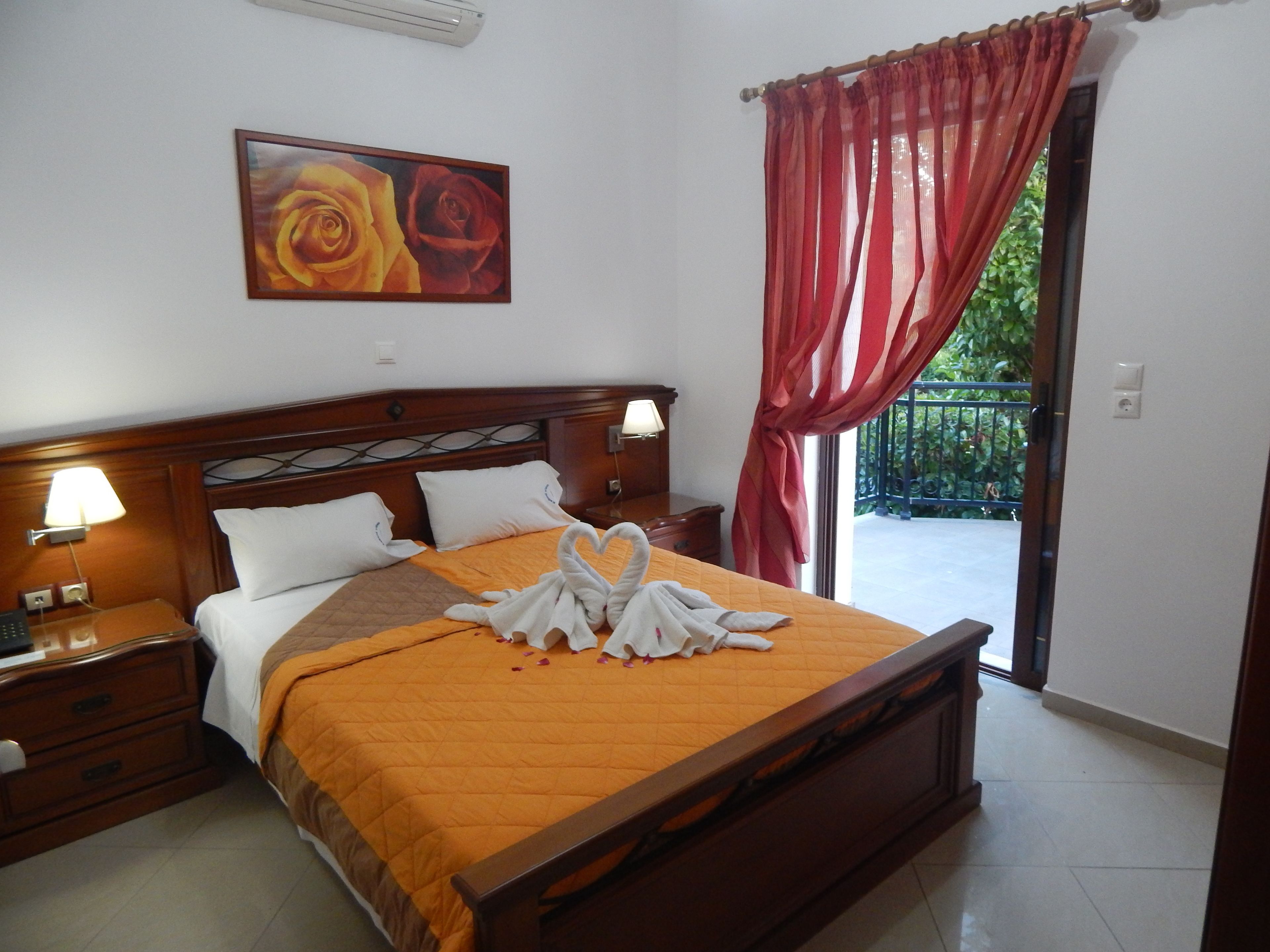A hotel room with a wooden bed, a painting of roses, a red curtain, and a balcony view.