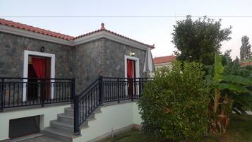 Un edificio de piedra con techo de tejas rojas, una escalera con barandillas negras y un pequeño jardín con farol.