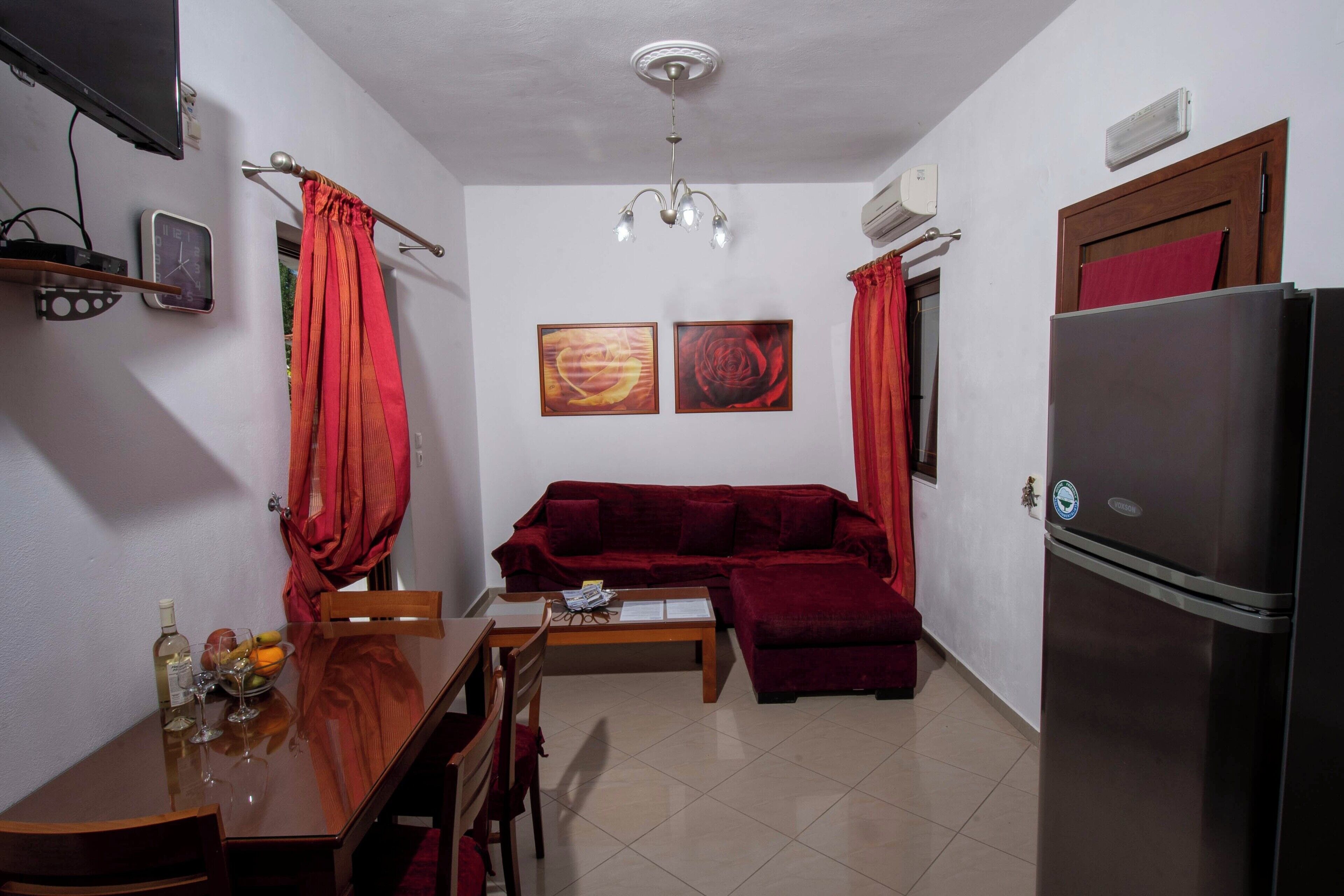 A compact living space with a sofa, dining table, chairs, a refrigerator, a TV, and artwork on the walls.