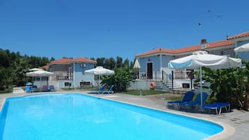 A swimming pool with lounge chairs and umbrellas, surrounded by buildings with red-tiled roofs.