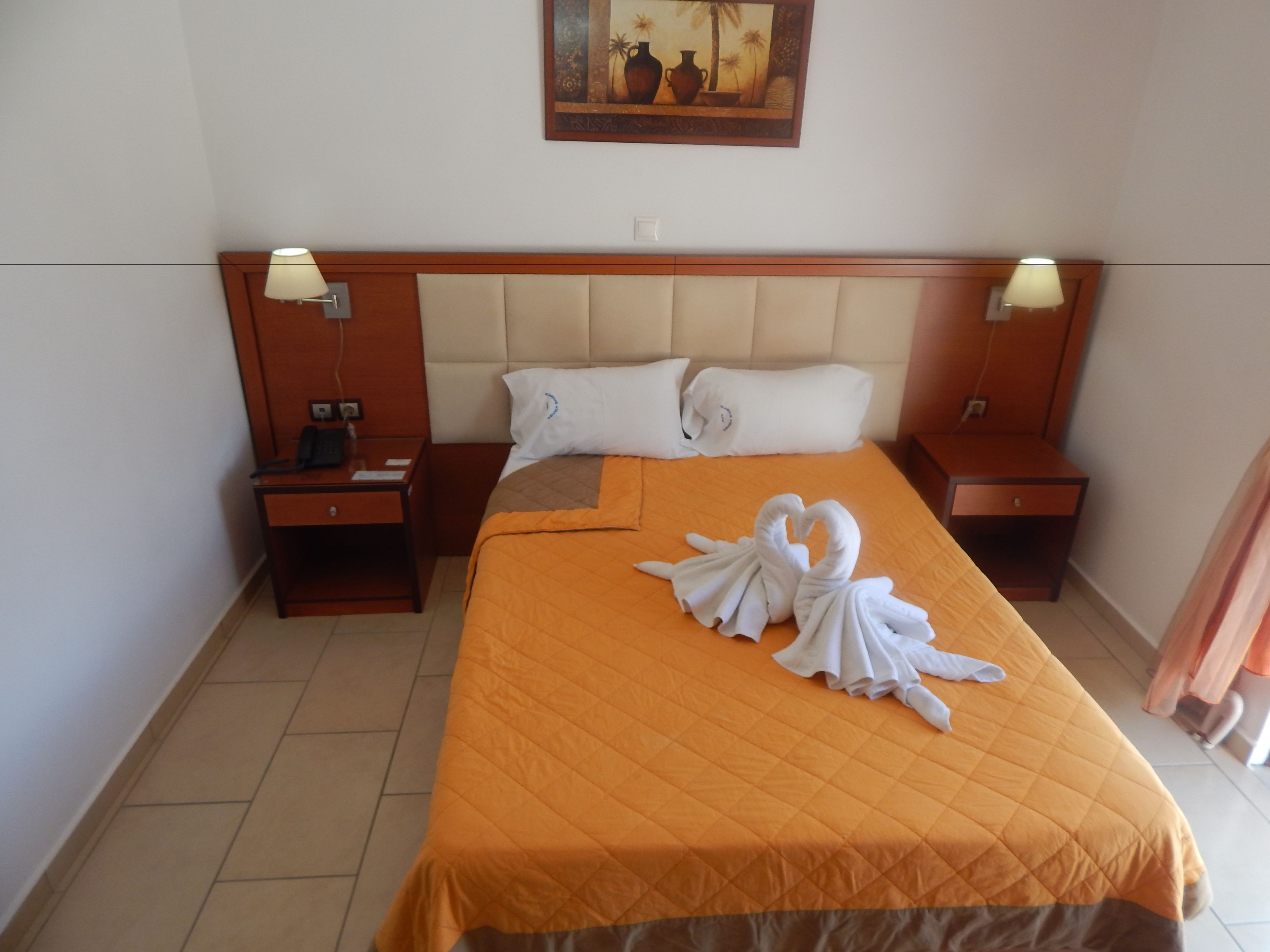 Habitación de hotel con una cama grande, dos mesitas de noche, un cuadro en la pared y una escultura de toallas en la cama.