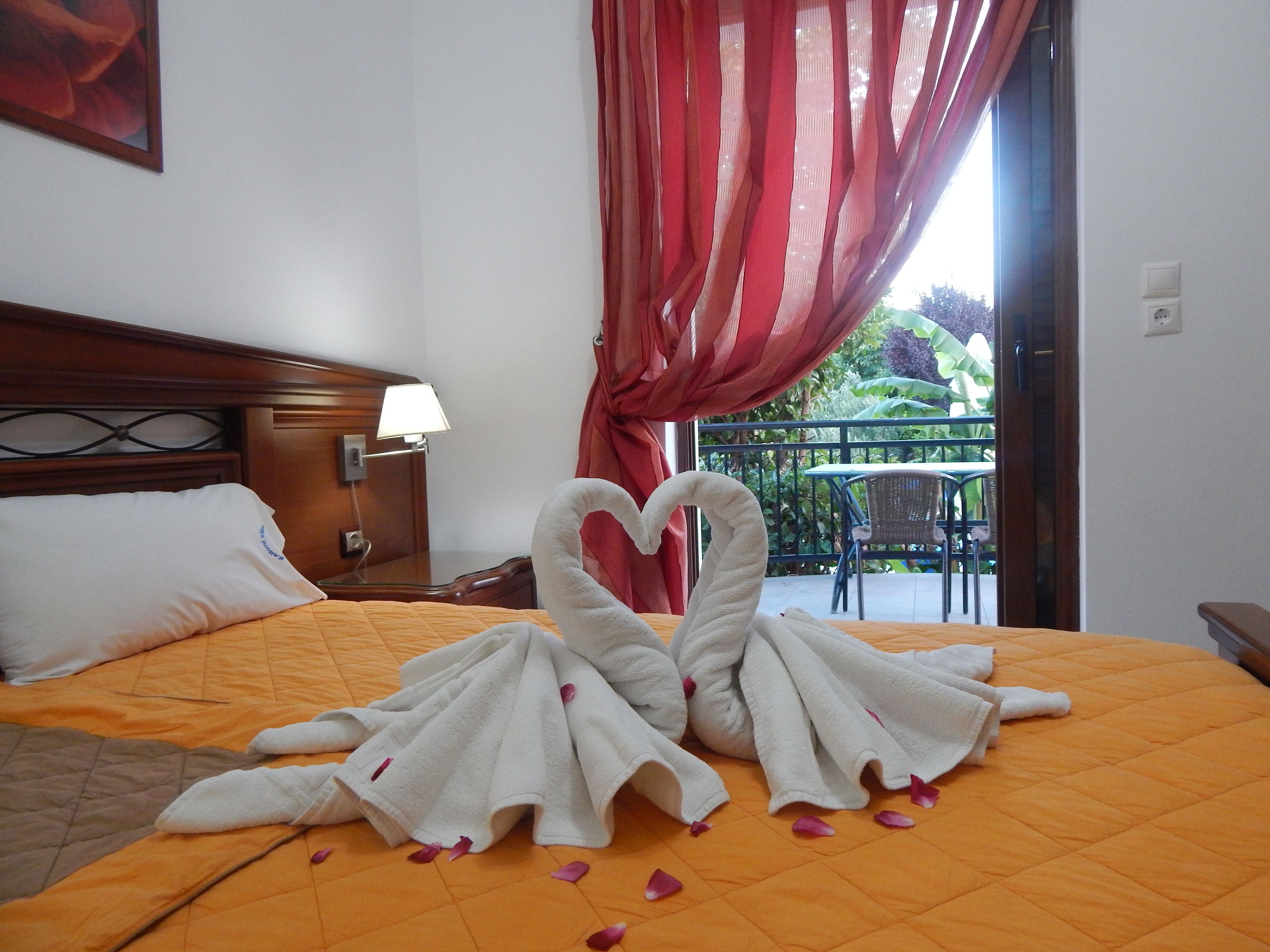 A hotel room with a bed, a nightstand, a lamp, and a view of a balcony with outdoor furniture.