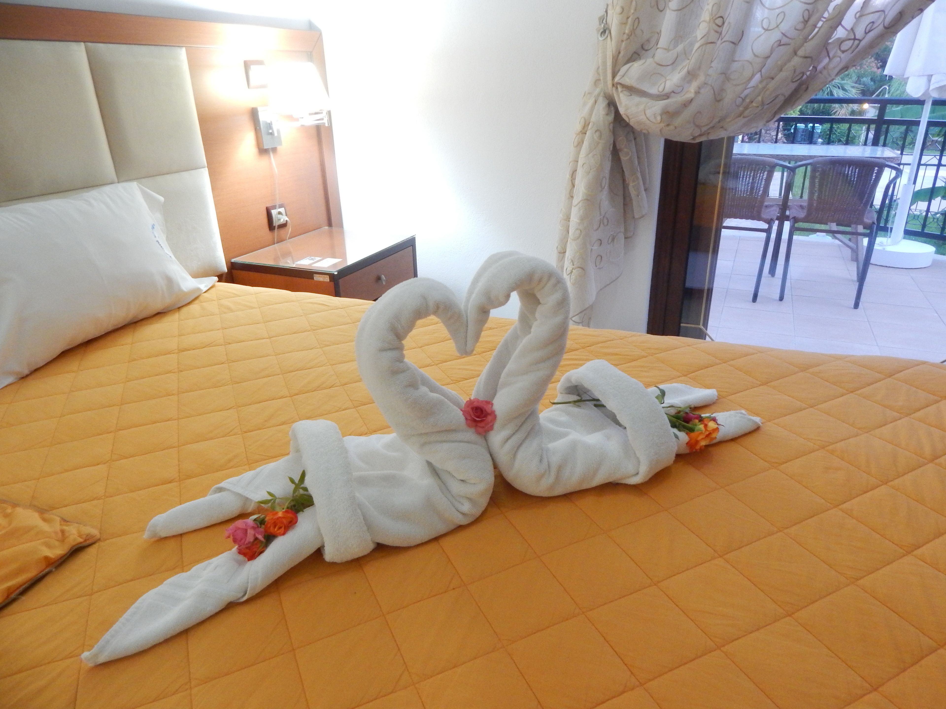 Ein Hotelzimmer mit einem Bett, dekoriert mit zwei schwanenförmigen Handtüchern und einem Blumenstrauß.