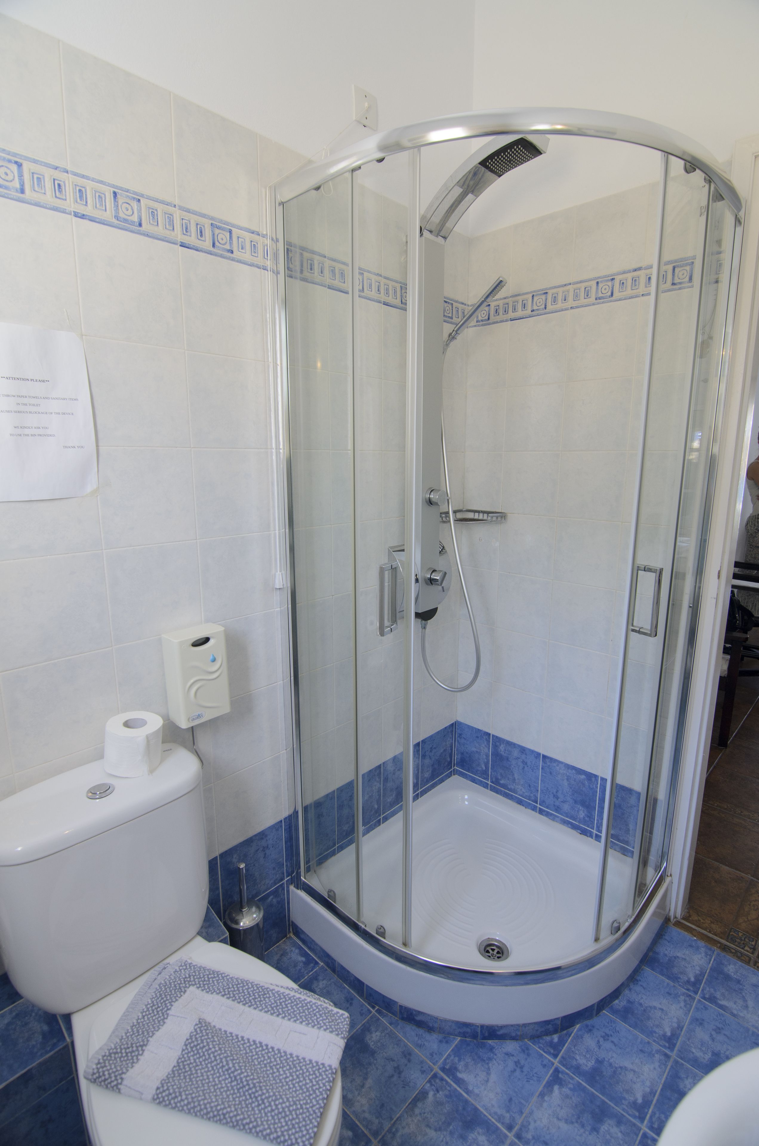 A glass-enclosed shower stall with a white toilet and blue-tiled walls.