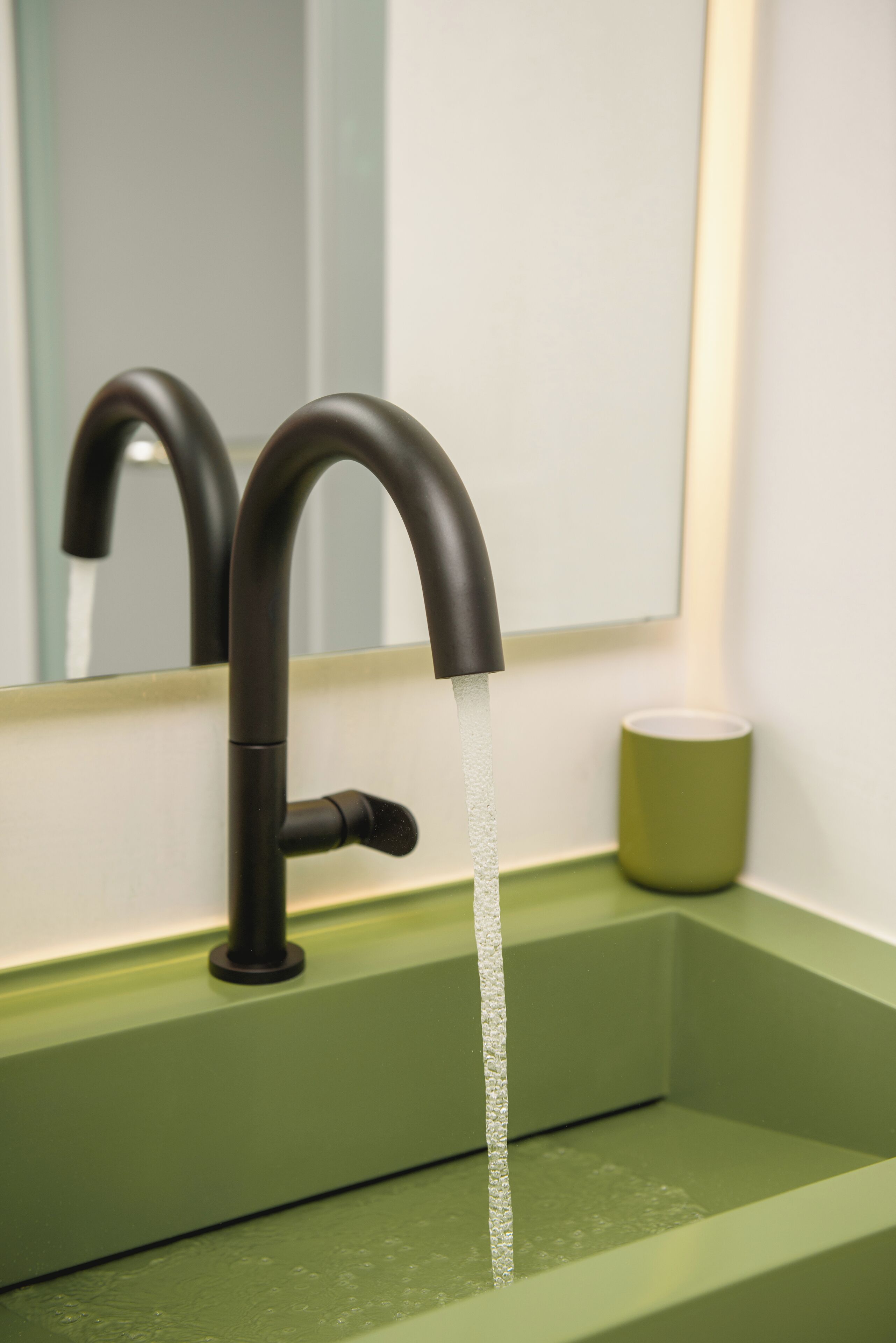 A modern bathroom sink with a green countertop and a black faucet.