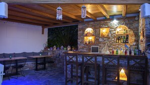 Zona de bar al aire libre con paredes de piedra, mobiliario de madera y lámparas colgantes.