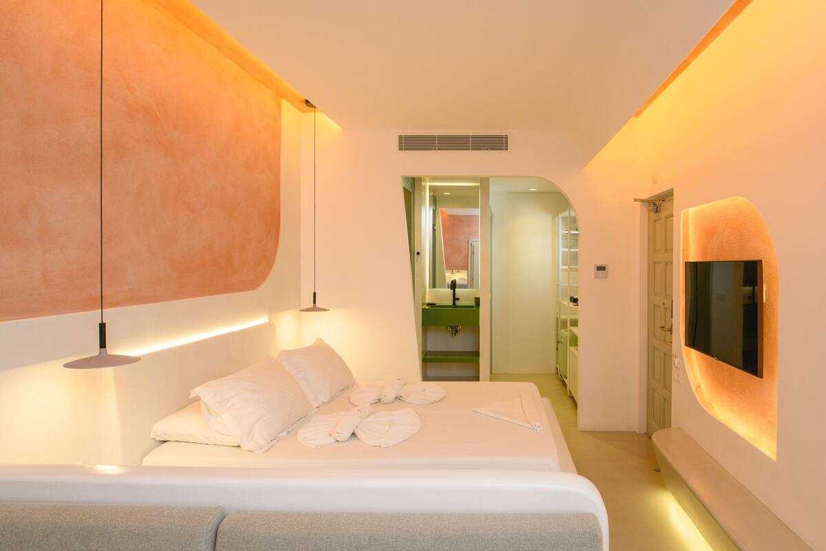 A modern hotel room with a large bed, bedside lamps, a TV, and a bathroom visible through an open door.