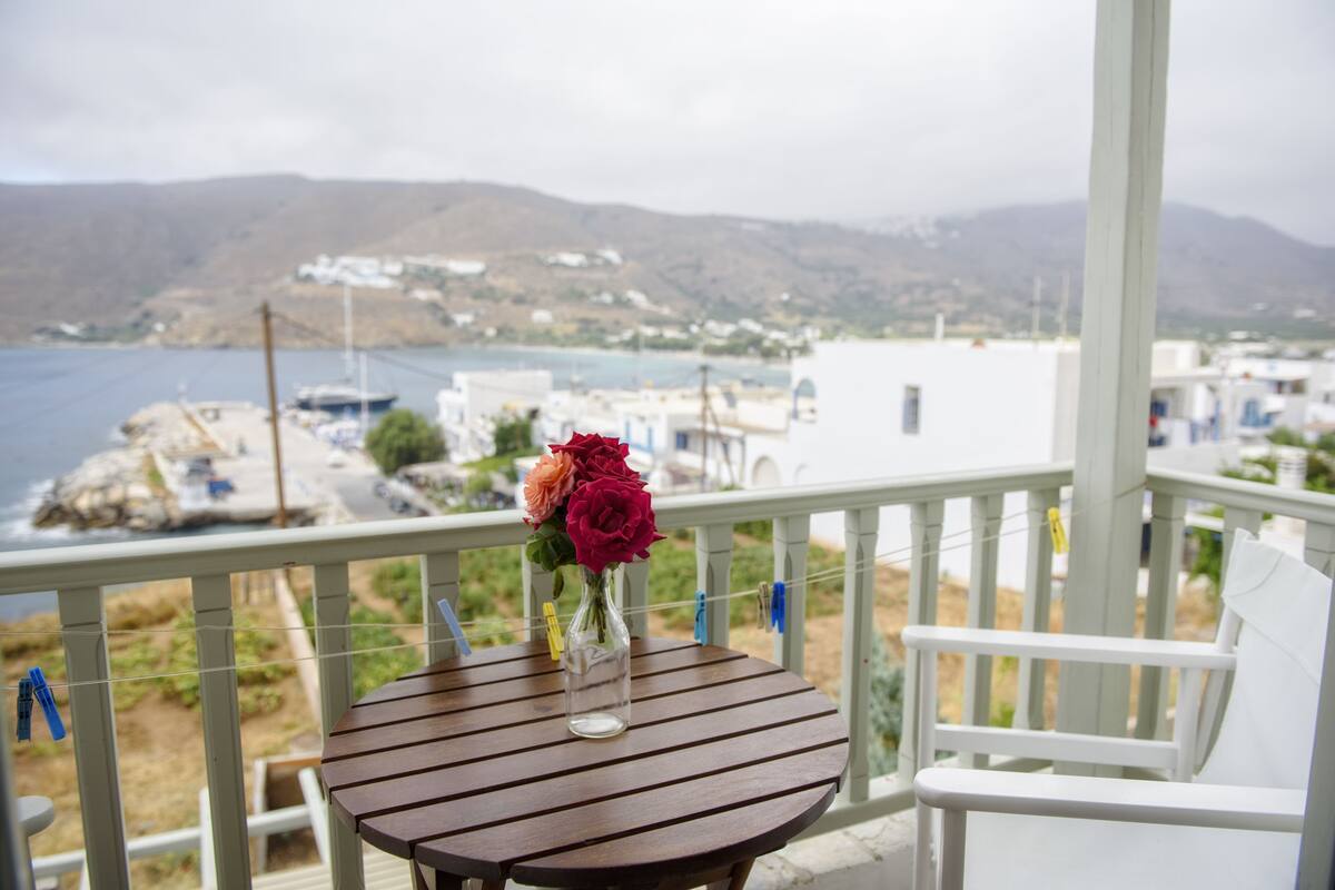 A wooden table with a vase of flowers on a balcony overlooking a coastal town.