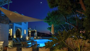 Un área de piscina con sillones de descanso y sombrillas, un muro de piedra y vistas al cielo nocturno.