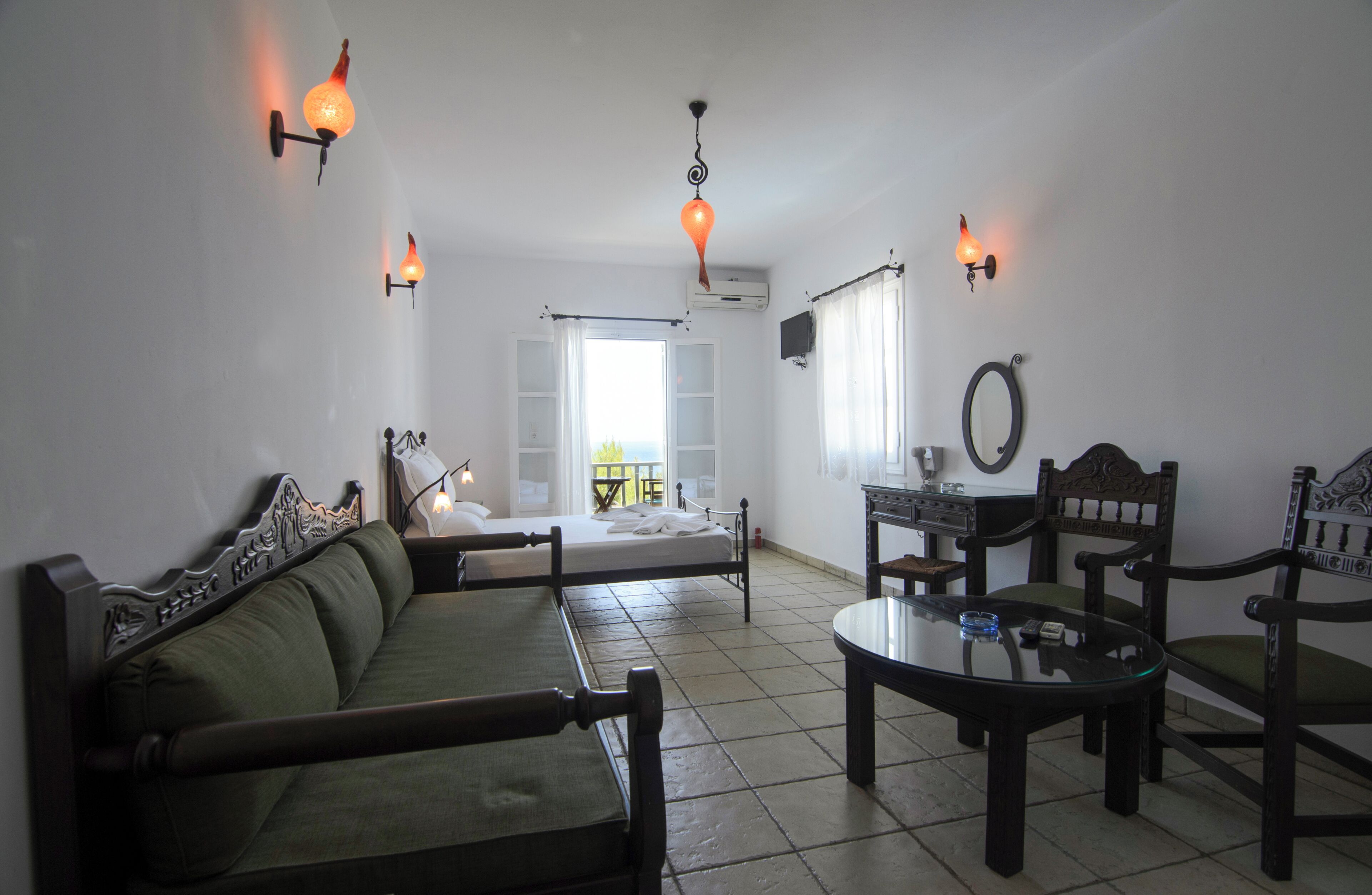 Una habitación con sofá, mesa, sillas, luces fijadas a la pared y ventana con cortinas.