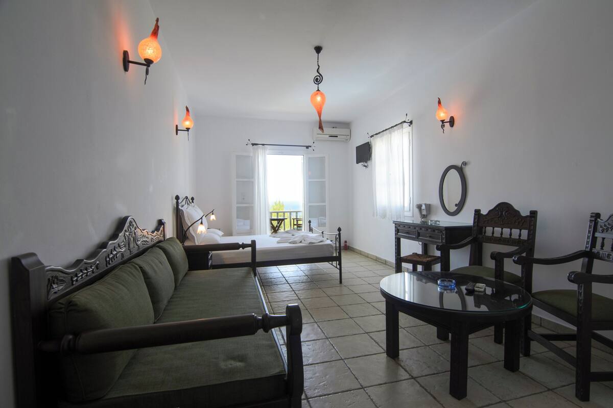 A room with a sofa, a table, chairs, wall-mounted lights, and a window with curtains.