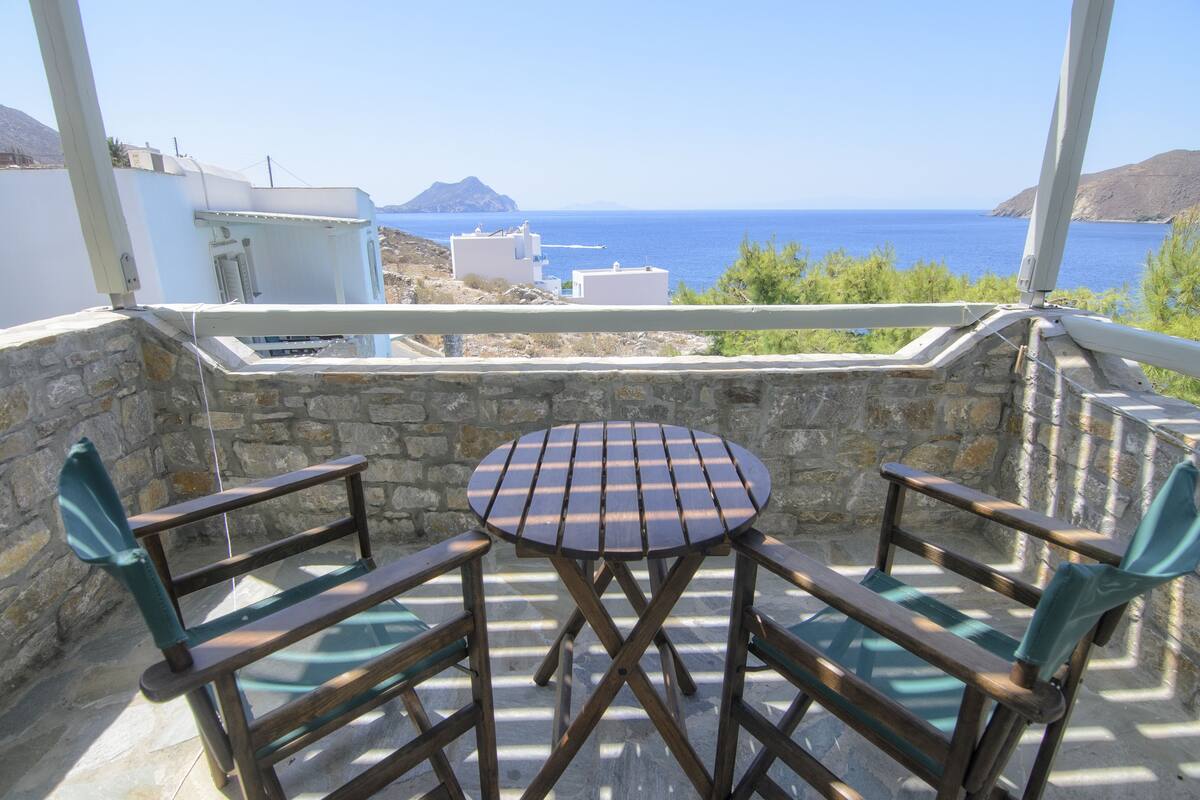 A balcony with a table and two chairs, overlooking a coastal view with buildings and the sea.