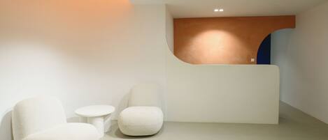 A modern reception area with a curved reception desk, two white armchairs, and a small round table.