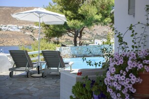 A poolside area with lounge chairs, a white umbrella, and a view of a hillside with buildings.