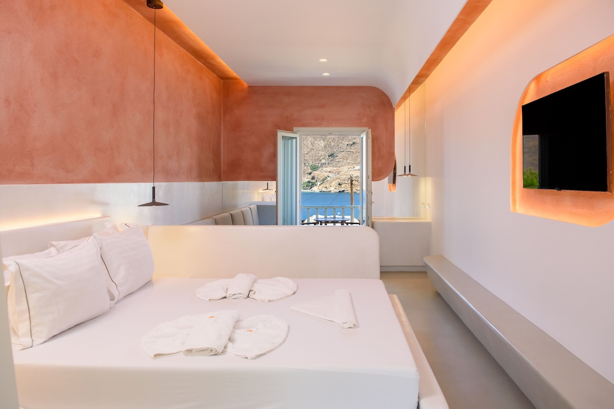 Une chambre d’hôtel moderne, dotée d’un lit, d’une vue sur la mer et d’un téléviseur fixé au mur.
