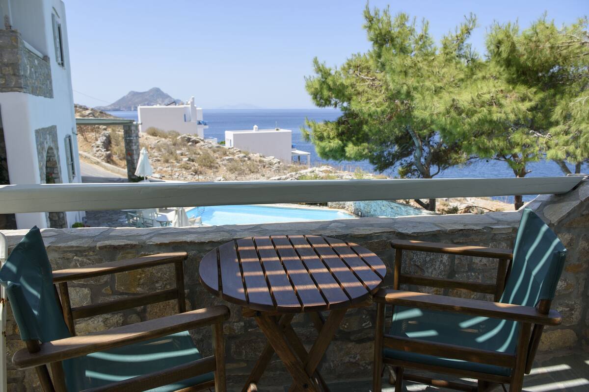A balcony with a table and chairs overlooking a pool and a mountainous landscape.