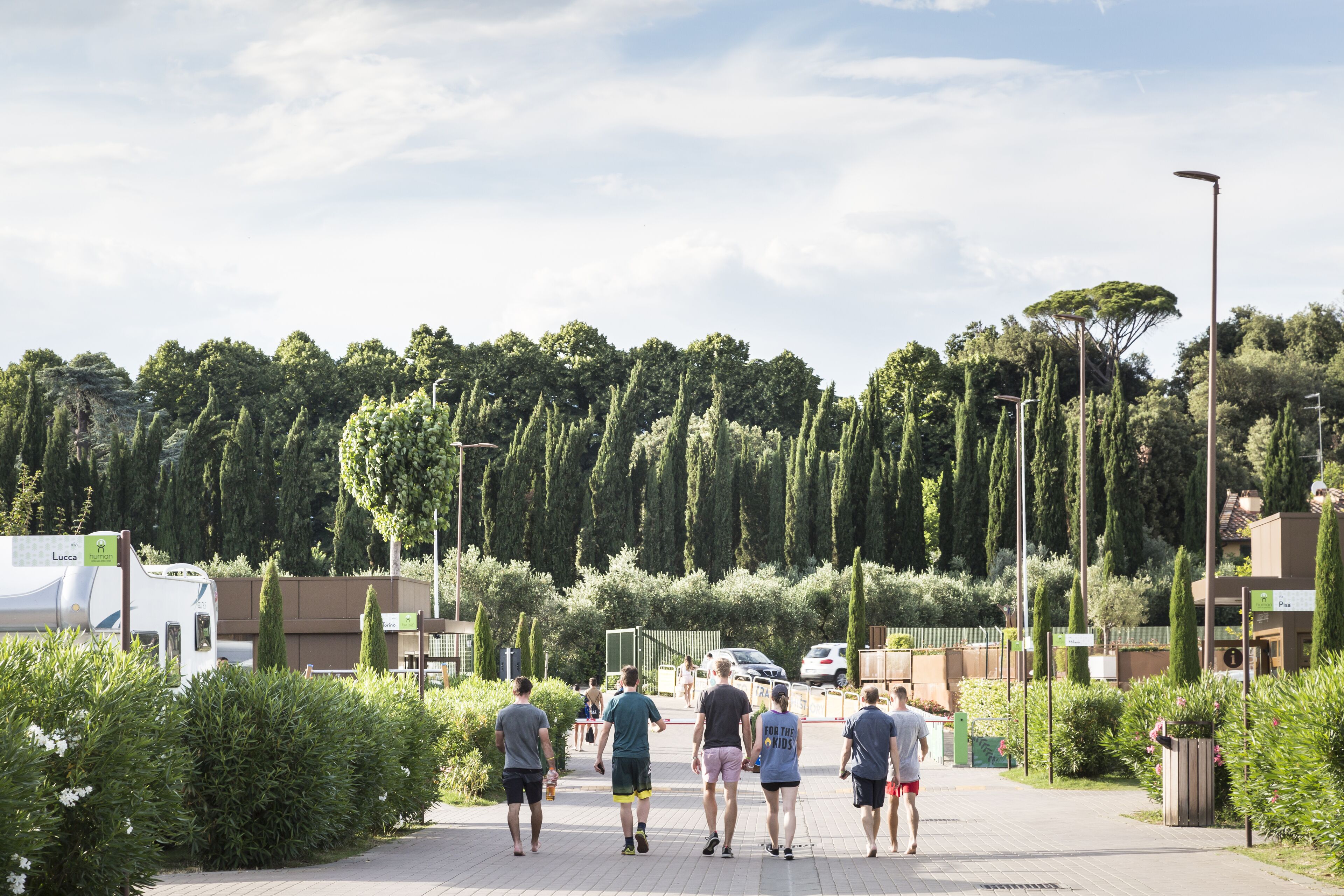 A group of people walking on a paved path in a park-like setting with trees and greenery.
