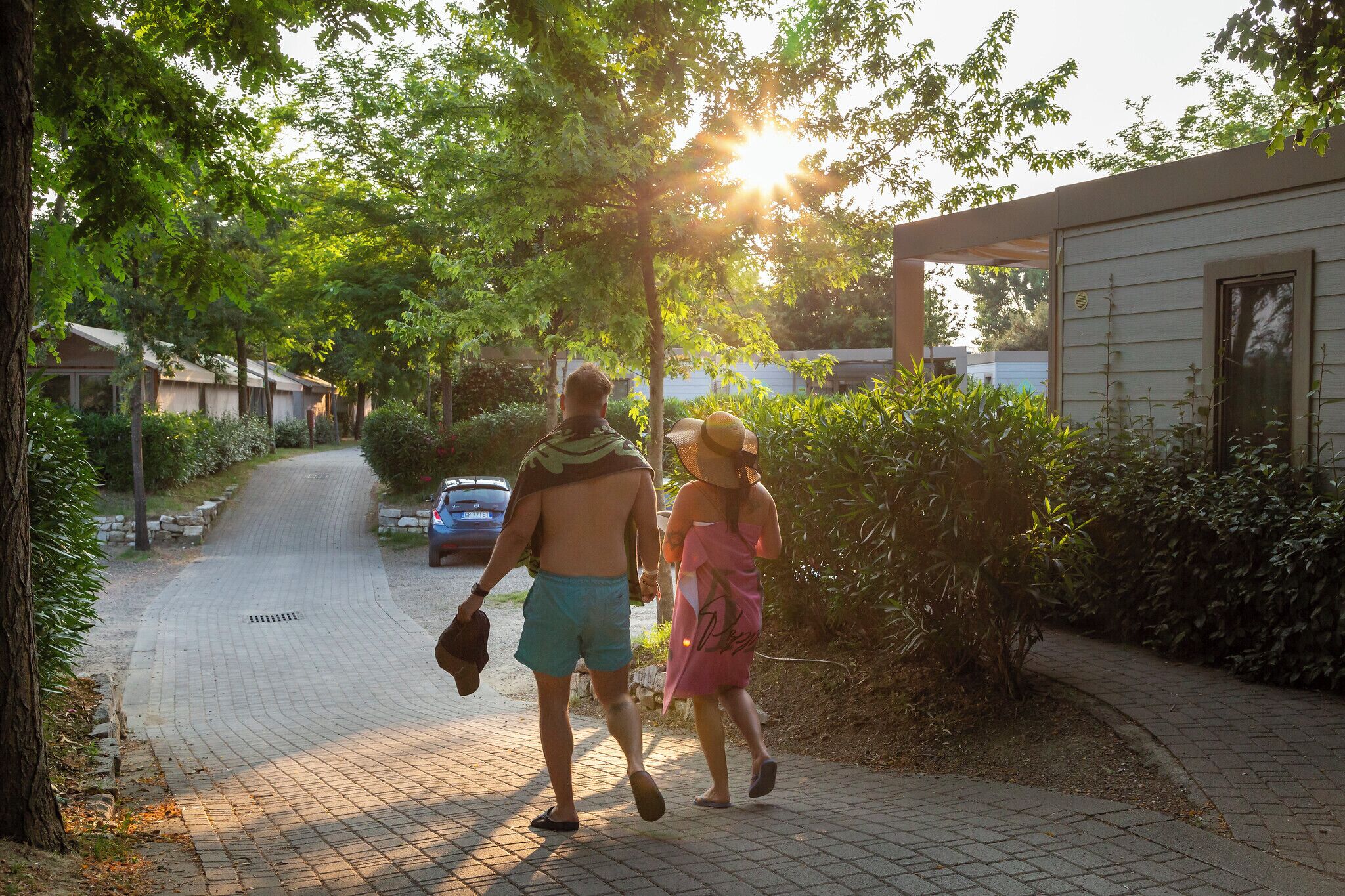 A couple walking on a paved path in a residential area with houses and greenery.