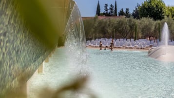 Zona de piscina amb aigua cristal·lina, una font i gandules blanques.