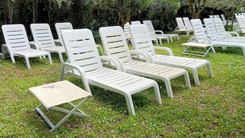 Seients de relaxació exteriors disposats per files sobre una zona verda, amb vegetació abundant al fons.