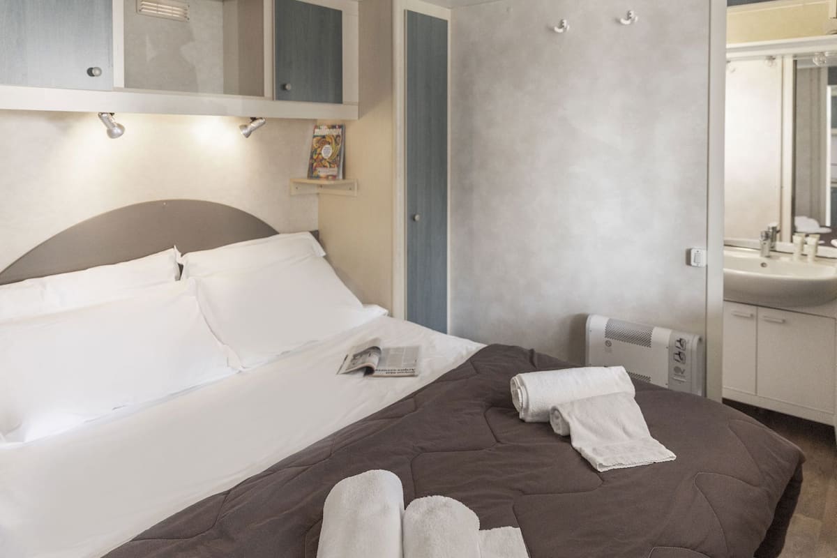 A hotel room with a bed, a bedside table, a mirror, a towel, and a heater.
