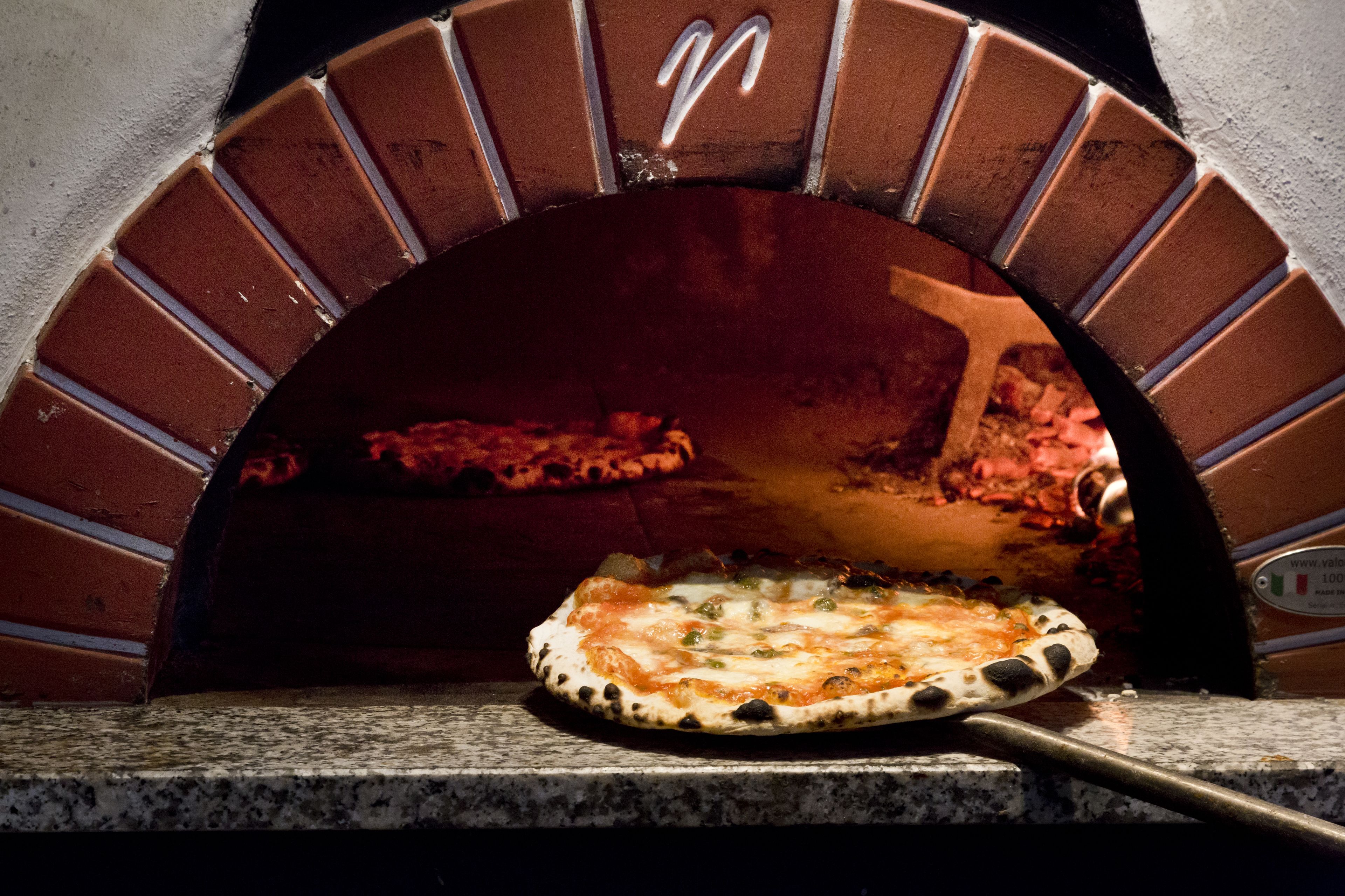 Un horno de pizza con arco de ladrillo y una pizza en su interior.