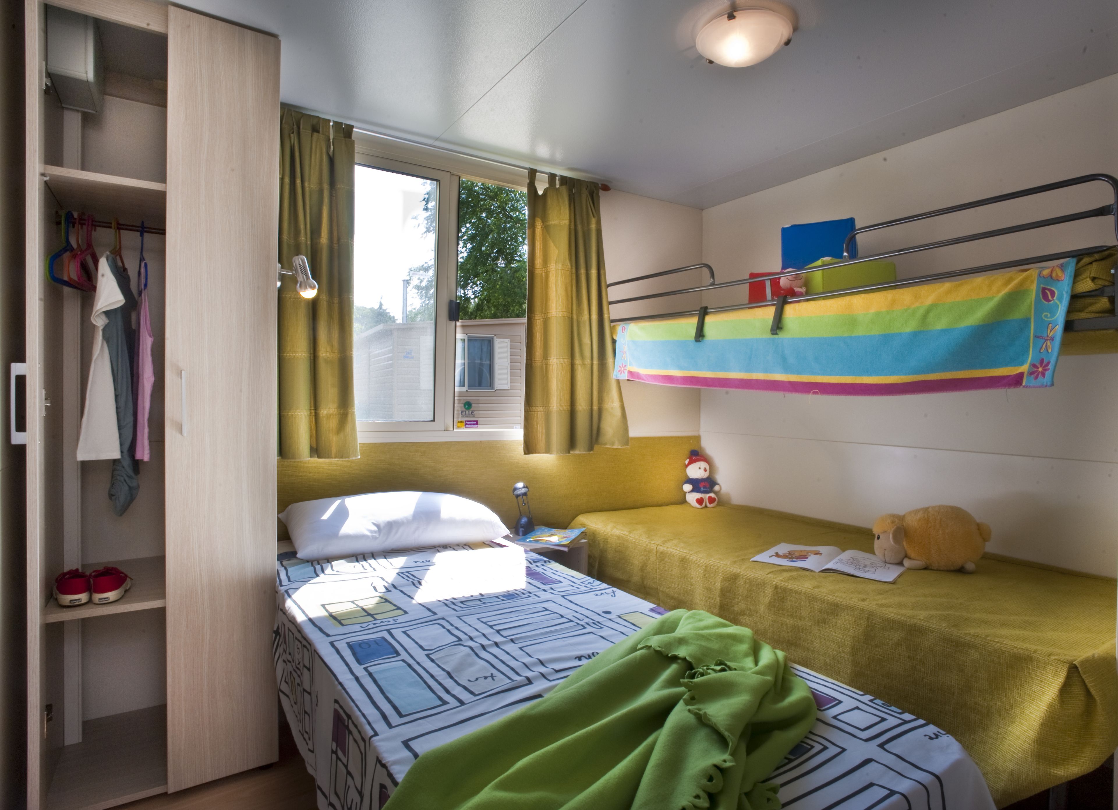 A dorm-style room with bunk beds, a wardrobe, and a window with curtains.