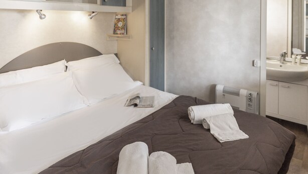 Ein Hotelzimmer mit einem Bett, einem Nachttisch, einem Heizkörper, einem Spiegel und einem Badezimmer mit einem Waschbecken.