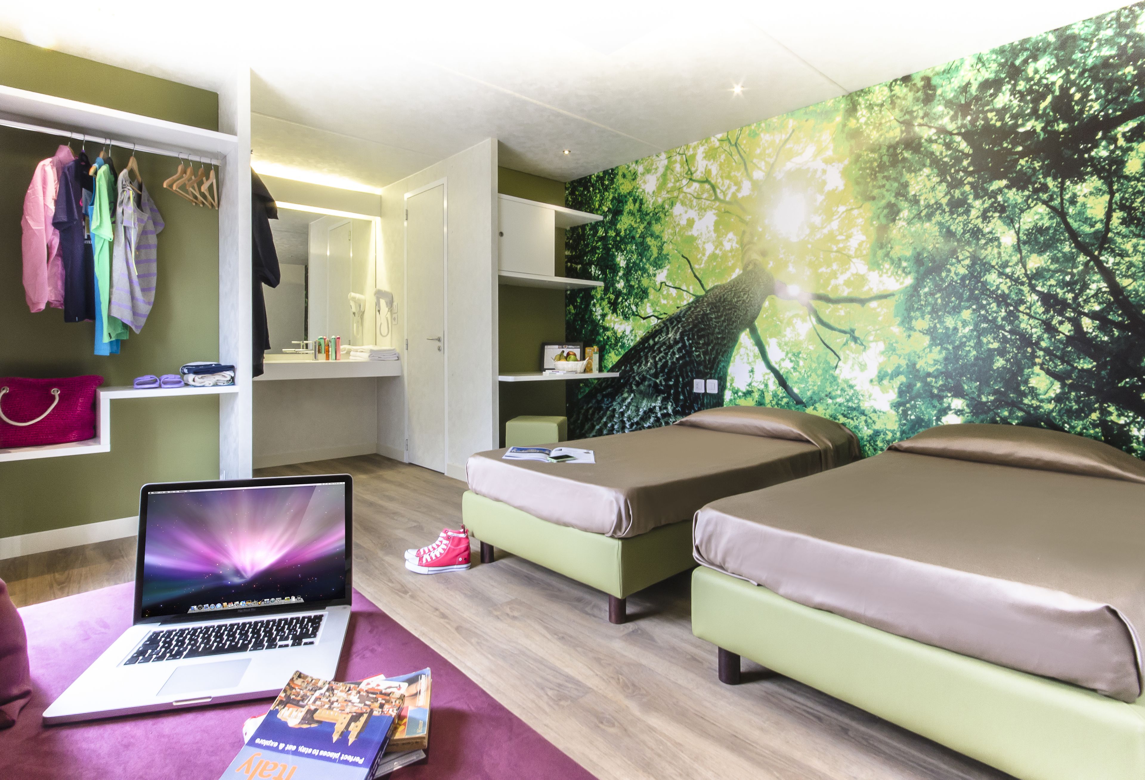 A modern bedroom with two beds, a laptop, and a bookshelf.