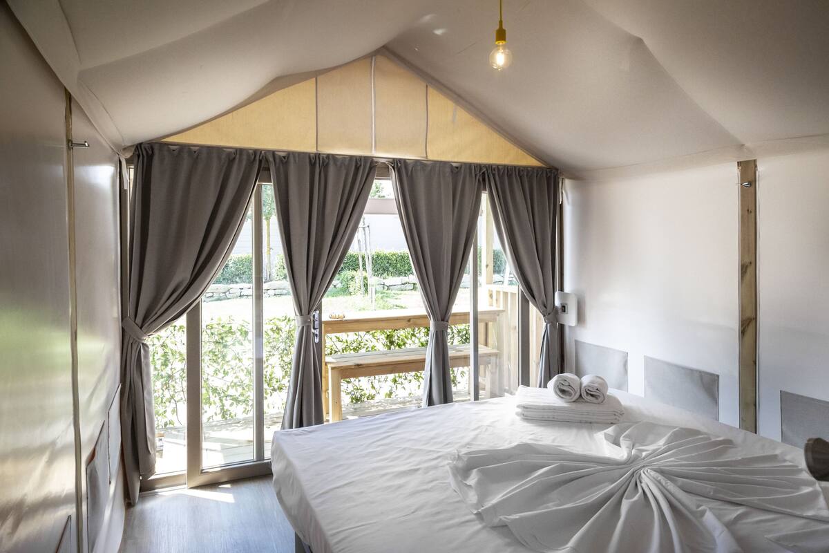 A bedroom with a large bed, curtains, and a view of greenery outside.