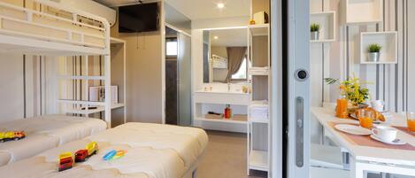 A hotel room with a bunk bed, a desk with breakfast items, and a bathroom with a mirror and shelves.