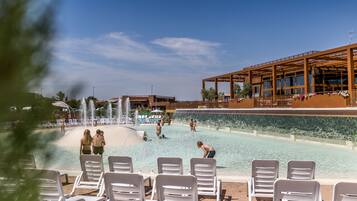 En swimmingpool med vandelementer, liggestole og en bygning med store vinduer.