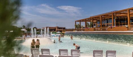 A swimming pool with water features, lounge chairs, and a building with large windows.