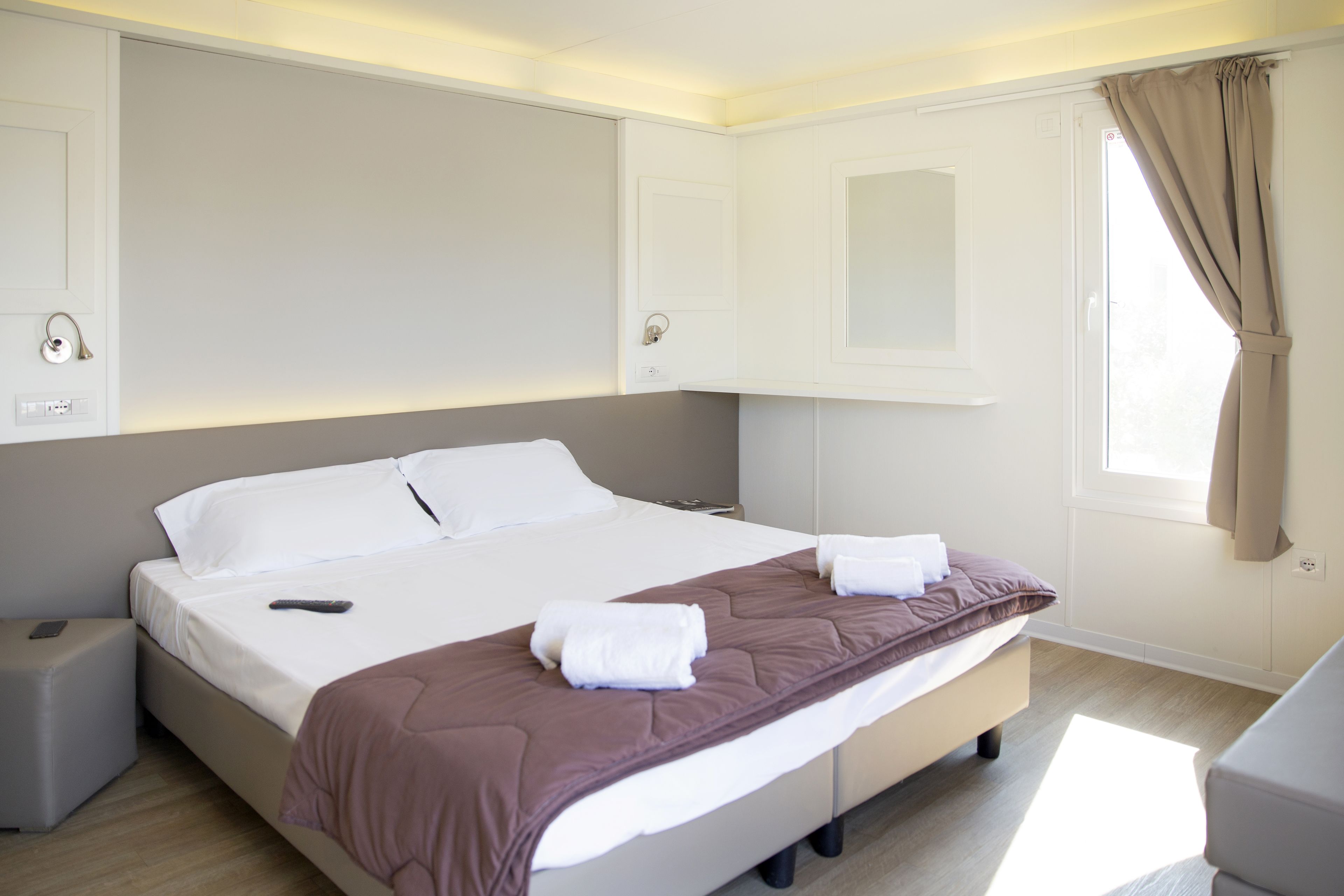 Una habitación de hotel moderna con una cama grande, mesitas de noche, una ventana con cortinas y armarios empotrados.