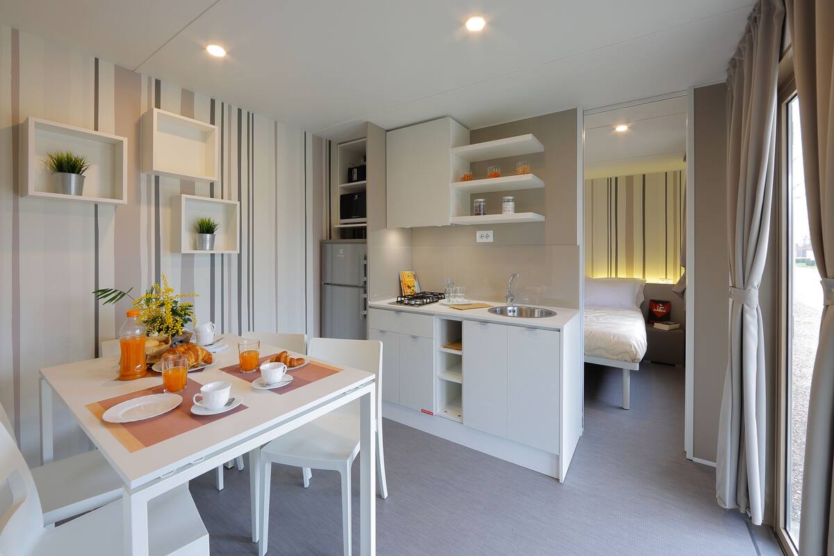A modern hotel room with a dining area, kitchenette, and a bed.