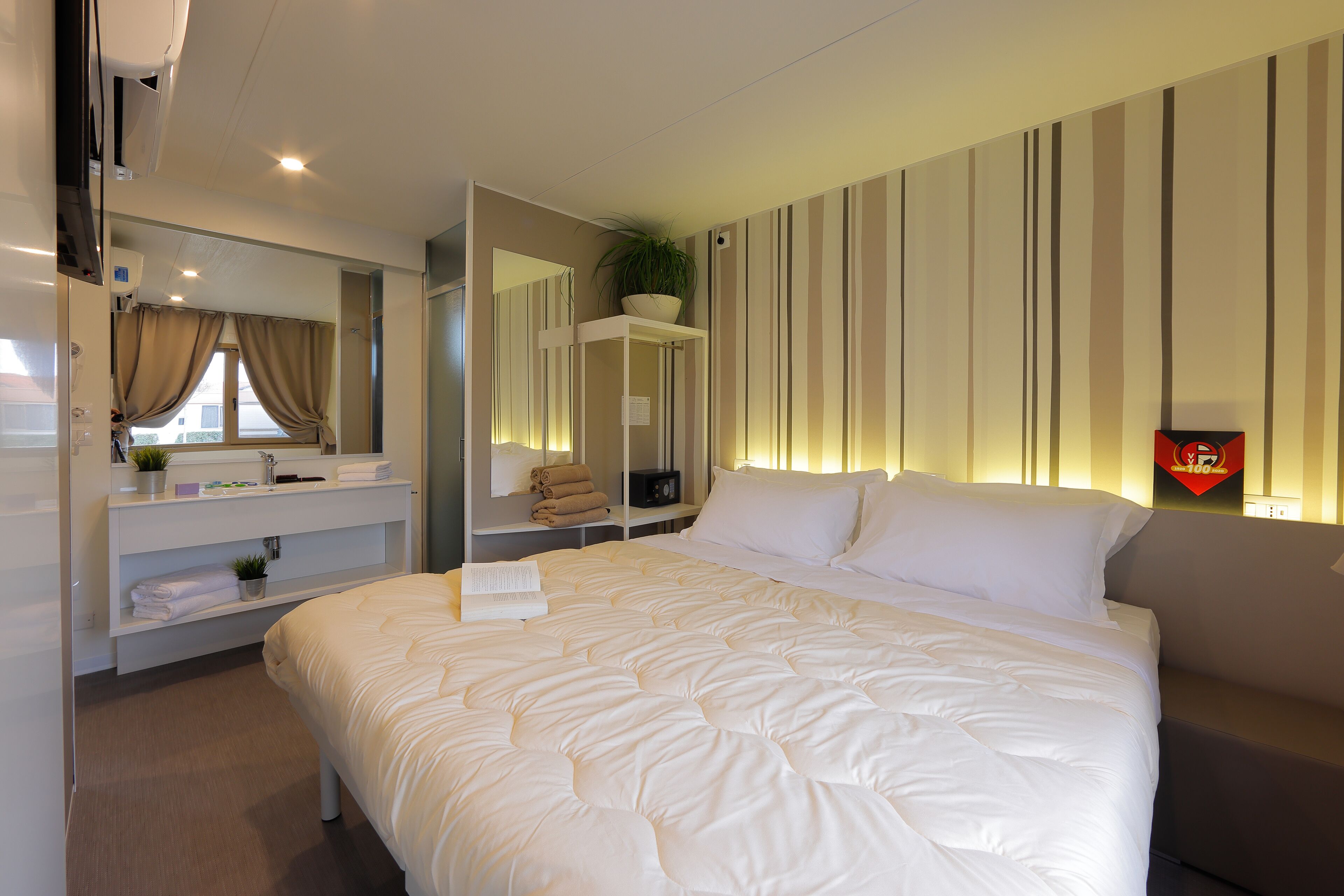 Une chambre d’hôtel avec un grand lit, une table de chevet agrémentée d’une plante, un miroir et un mur à rayures.