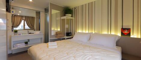 Una habitación de hotel con una cama grande, una mesita de noche con una planta, un espejo y una pared a rayas.