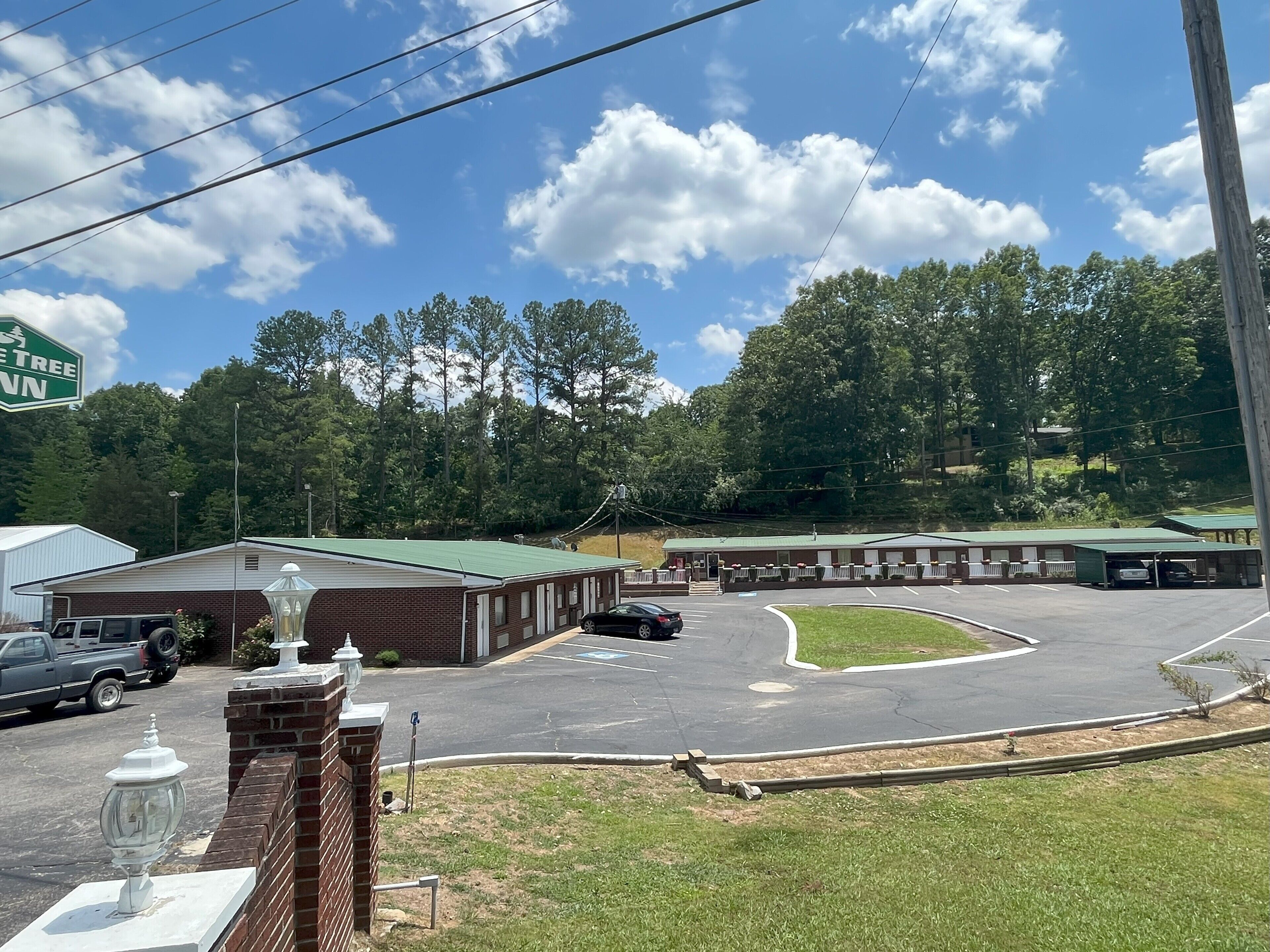 A motel with a green roof, a parking lot, and a wooded area in the background.