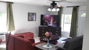 A living room with a television, red sofa, grey sofa, and a small table with a vase. - Pine Tree Inn (Parsons)