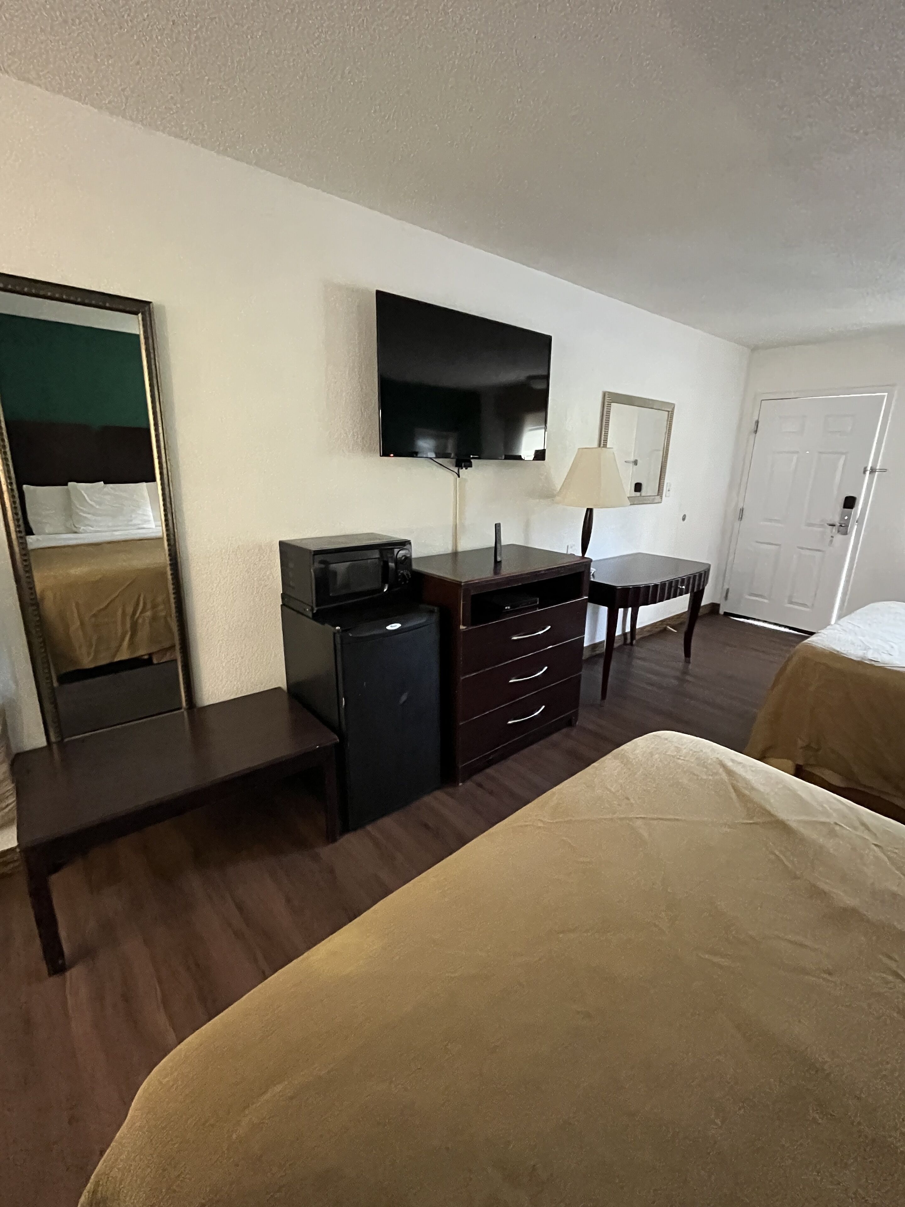 A hotel room with a bed, a dresser, a television mounted on the wall, a desk, and a chair.