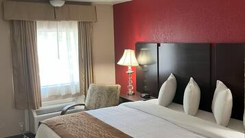 A hotel room with a large bed, a bedside table with a lamp, a chair, and a window with curtains.
