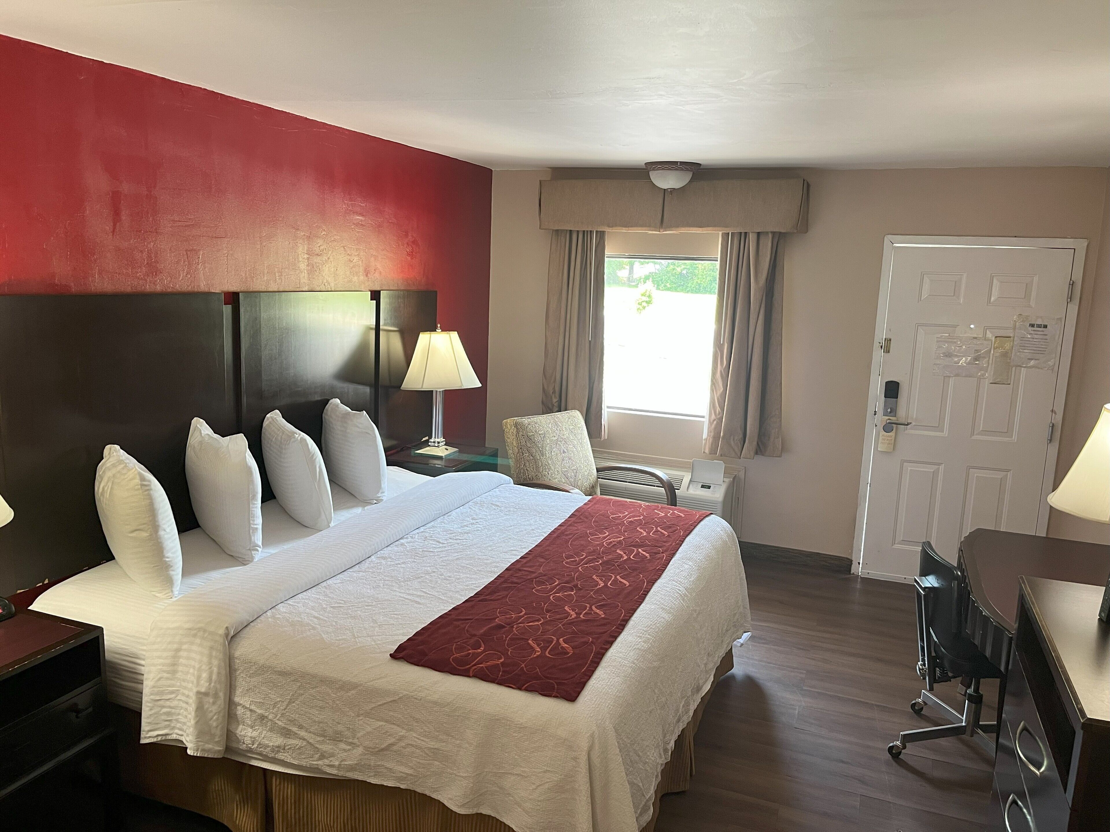 Habitación de hotel con una cama grande, un escritorio, una silla, un ventanal con cortinas y una puerta con cerradura.