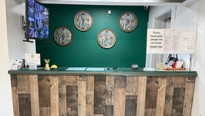 A reception desk with a green wall and wooden paneling, a security camera, decorative plates, a pet policy sign, and a payment terminal. - Pine Tree Inn (Parsons)