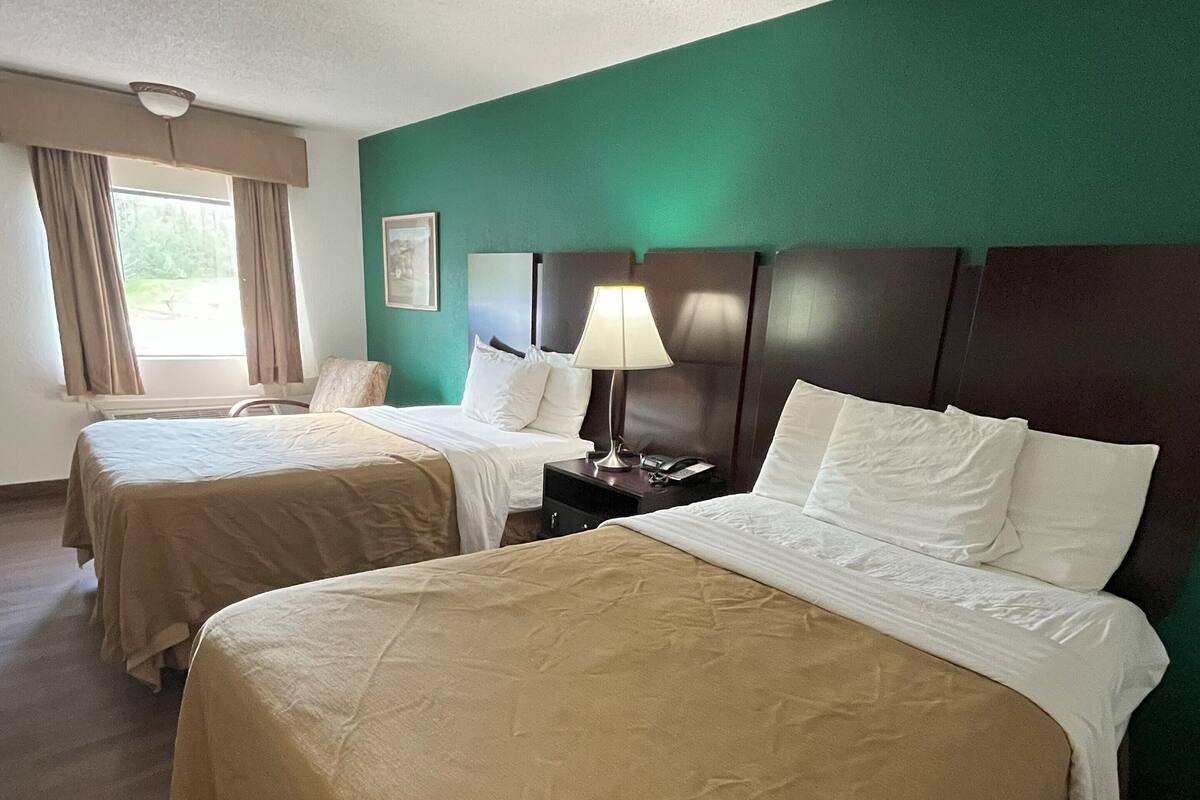 Une chambre d’hôtel avec deux lits, une table de chevet, une lampe et une fenêtre avec des rideaux.