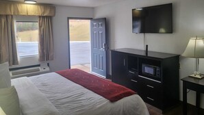 A hotel room with a bed, a TV, a desk, and a window with curtains. - Pine Tree Inn (Parsons)