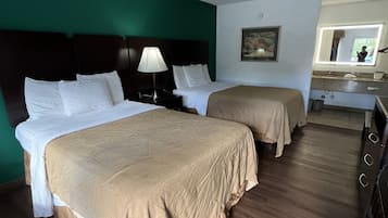 A hotel room with two beds, a nightstand with a lamp, a painting on the wall, and a bathroom visible through an open door.