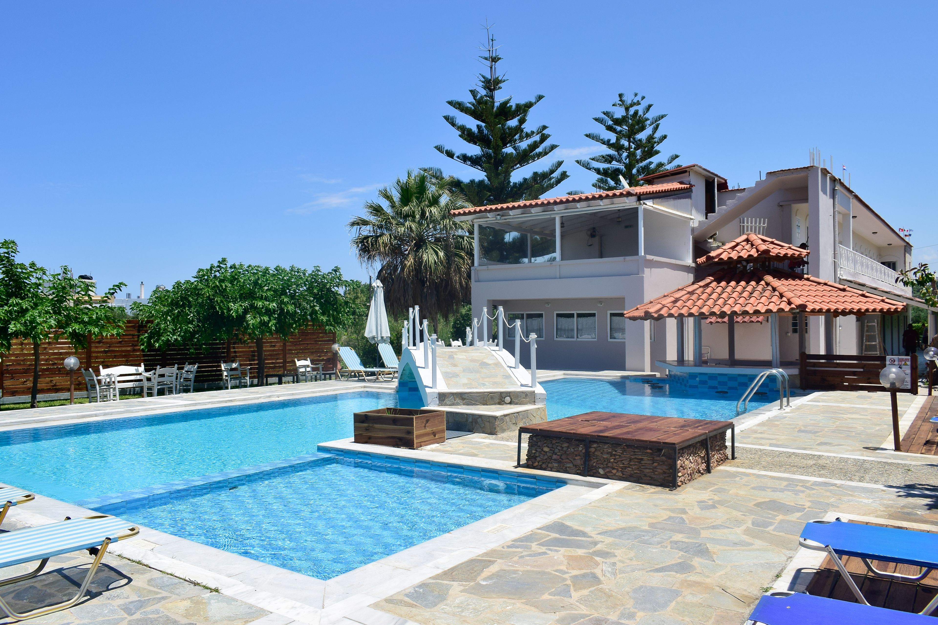 A swimming pool with lounge chairs, a wooden deck, and a building with a red-tiled roof.