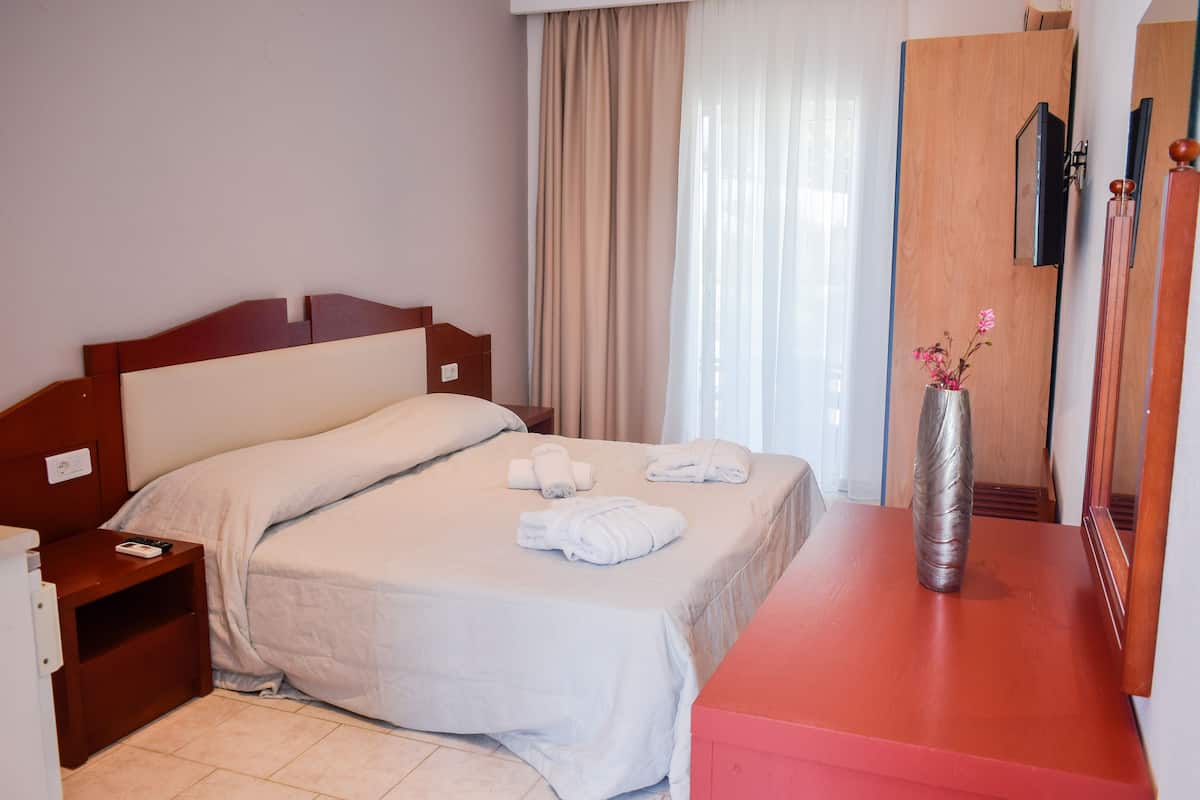 A hotel room with a bed, a nightstand, a dresser, a mirror, and a window with curtains.
